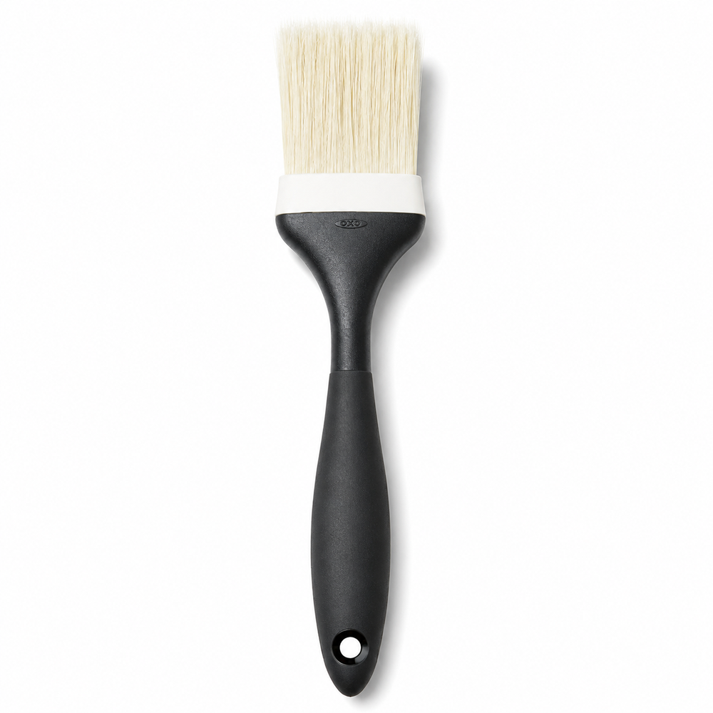 A kitchen brush with a matte black handle, a white ferrule, and cream-colored bristles, shown against a plain white background.