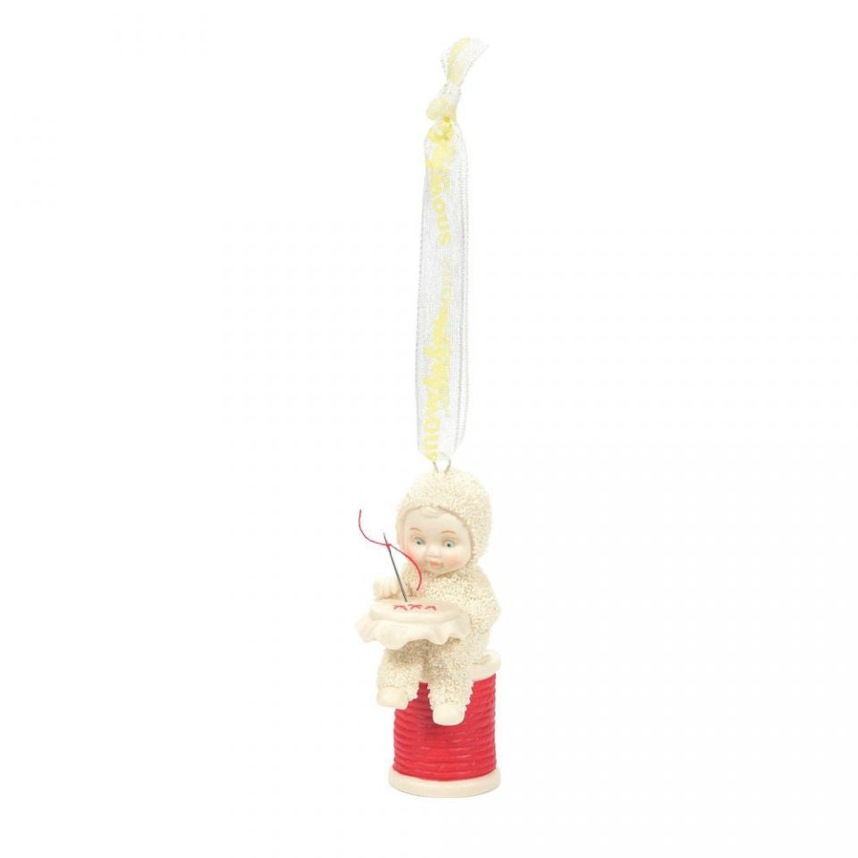 A Snowbabies ornament featuring a small figurine of a baby sitting on a red spool with a yellow string-like attachment, designed for Christmas decoration.