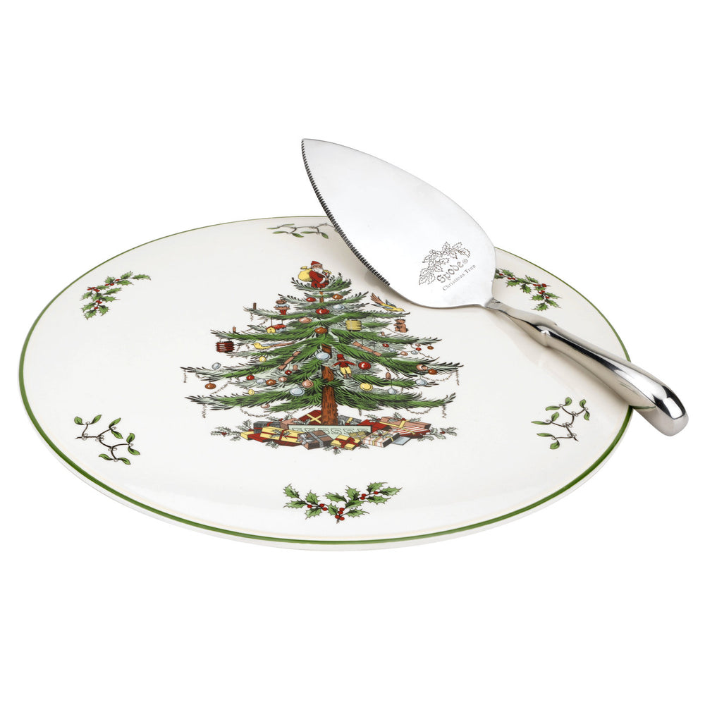 A decorative Christmas tree cake plate with a metallic server, featuring green and red holiday-themed decorations around the edge.