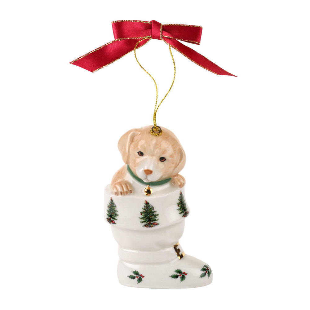 A ceramic Christmas ornament features a puppy peeking from a festive stocking adorned with trees. It hangs from a red ribbon, evoking holiday cheer.