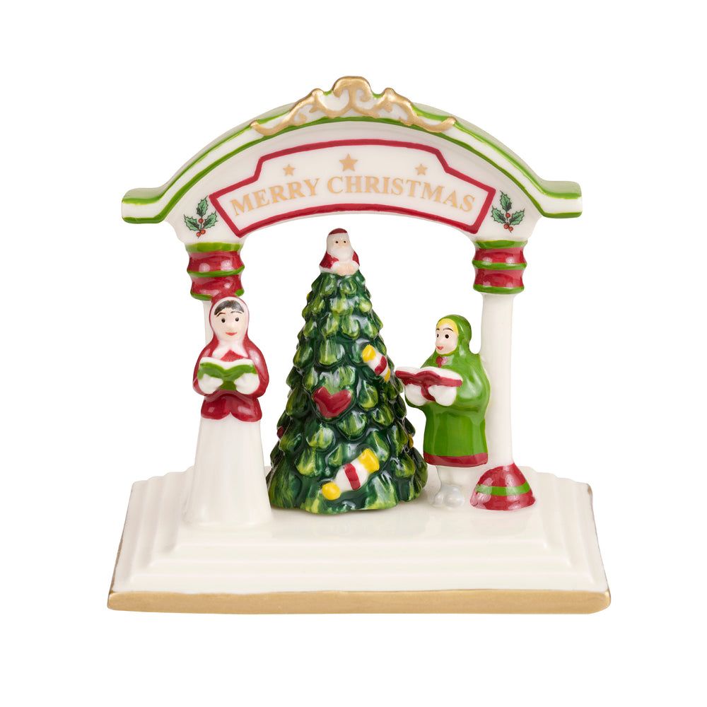 Ceramic Christmas decoration depicting carolers around a tree under an arch. The arch is decorated with holly and reads "Merry Christmas."