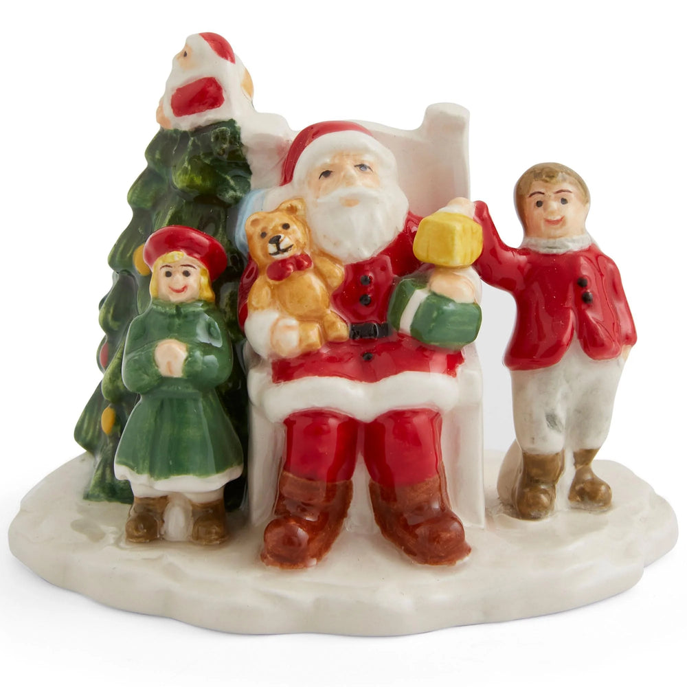 Ceramic figurine of Santa and two children. Santa, in red, holds gifts and a teddy bear. A girl in green and boy in red stand joyfully by a Christmas tree.