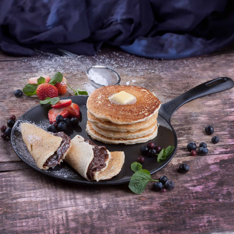 Stack of pancakes with butter, berries, and a side of crepes on a wooden table.