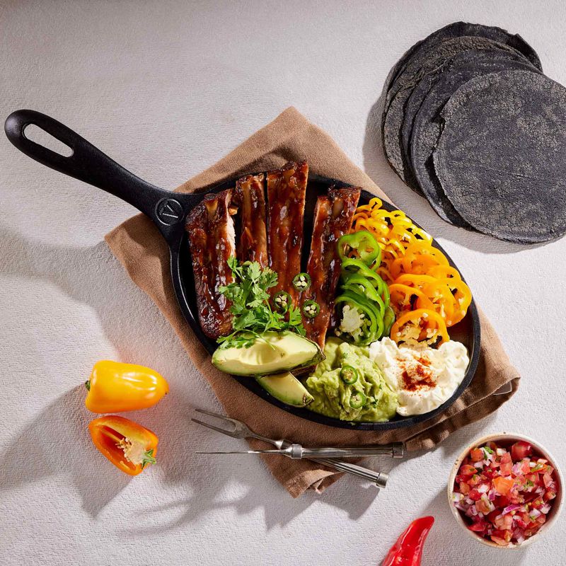 Skillet with grilled meat, vegetables, and tortillas on a light surface