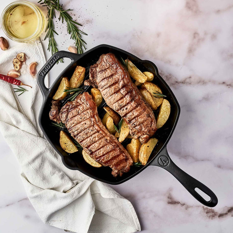 Steaks with potatoes in a cast iron skillet on a marble surface