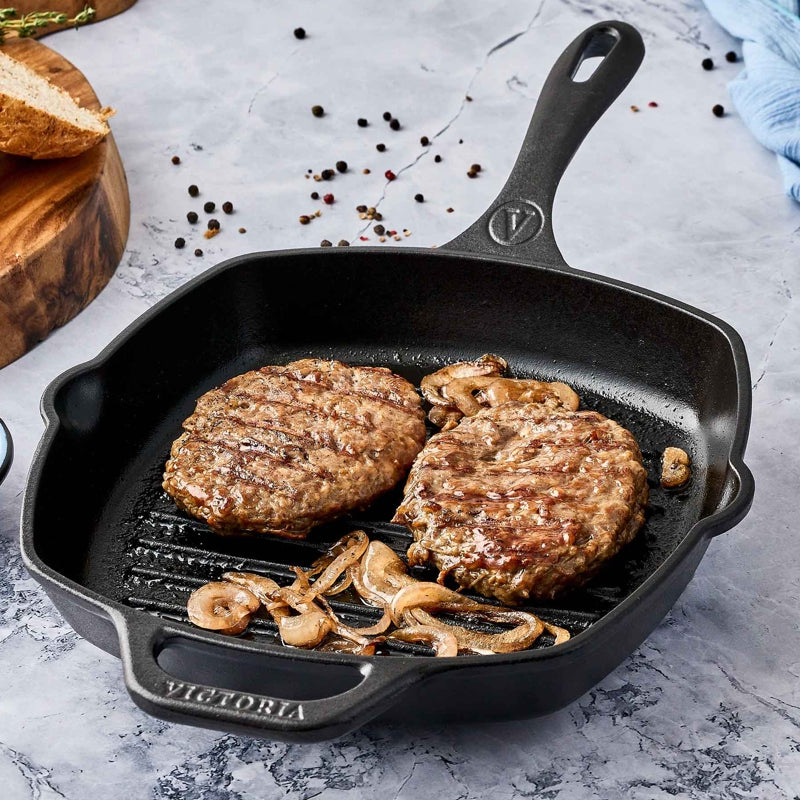 Two hamburger patties cooking in a black cast iron skillet on a gray surface.
