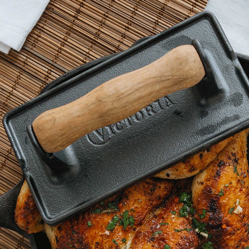 Black press with wooden handle on a grill with cooked chicken