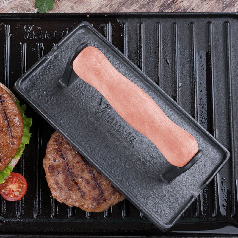 Hot dog in a black metal hot dog grill on a grill with burgers and vegetables.