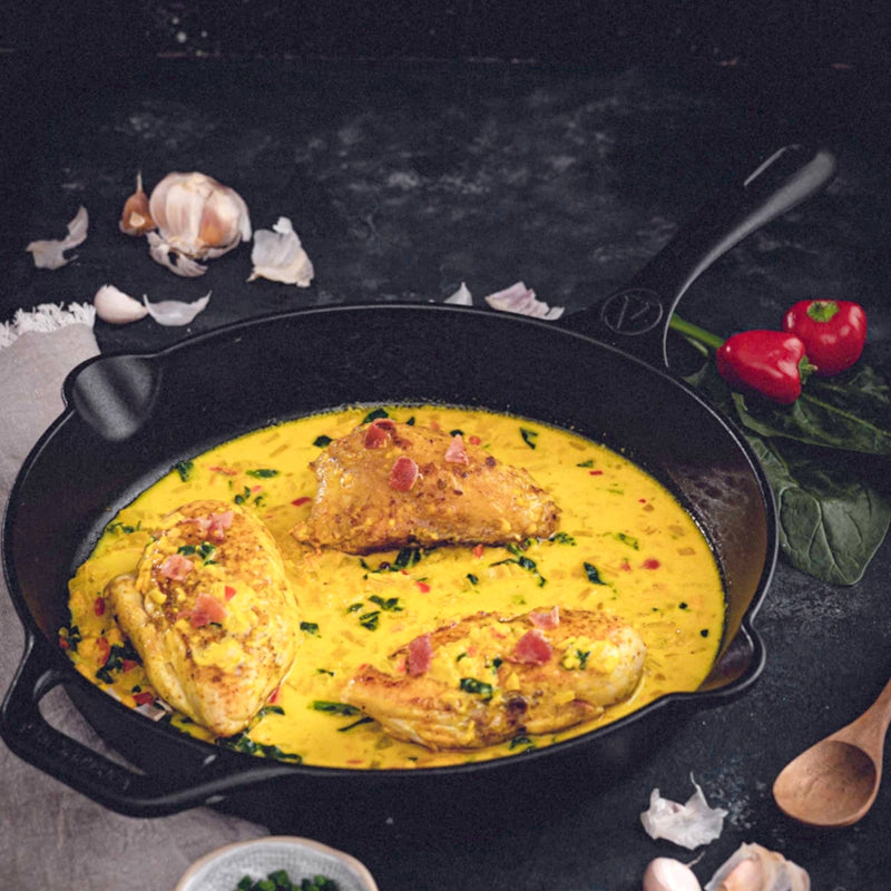 Yellow curry with chicken in a black cast iron skillet on a dark surface.