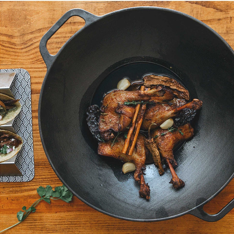 Roasted duck legs with herbs in a black cast iron skillet on a wooden surface.