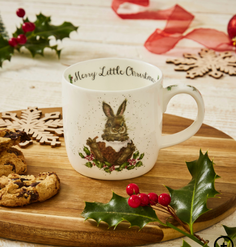 Christmas-themed mug with a rabbit design on a wooden surface with cookies and holly.