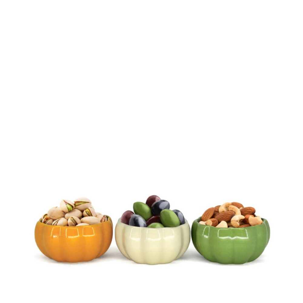 A set of three pumpkin-shaped stoneware bowls in orange, beige, and green colors, each bowl filled with various nuts and fruits.