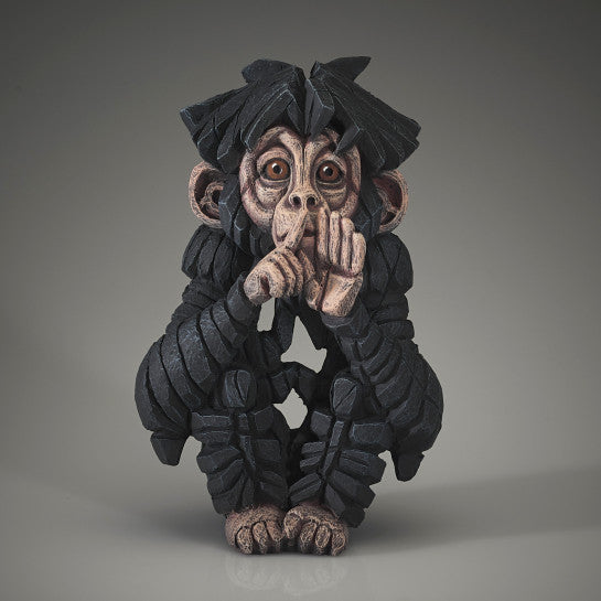 A sculpture of a baby chimpanzee with a playful expression, sitting with its fingers to its mouth.